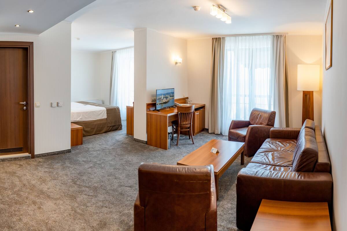 A hotel room with a bed, a desk with a chair, a sofa, a coffee table, and a TV.