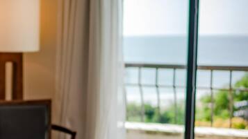 Una habitación con vista al mar, una ventana con cortinas y una mesa con lámpara.