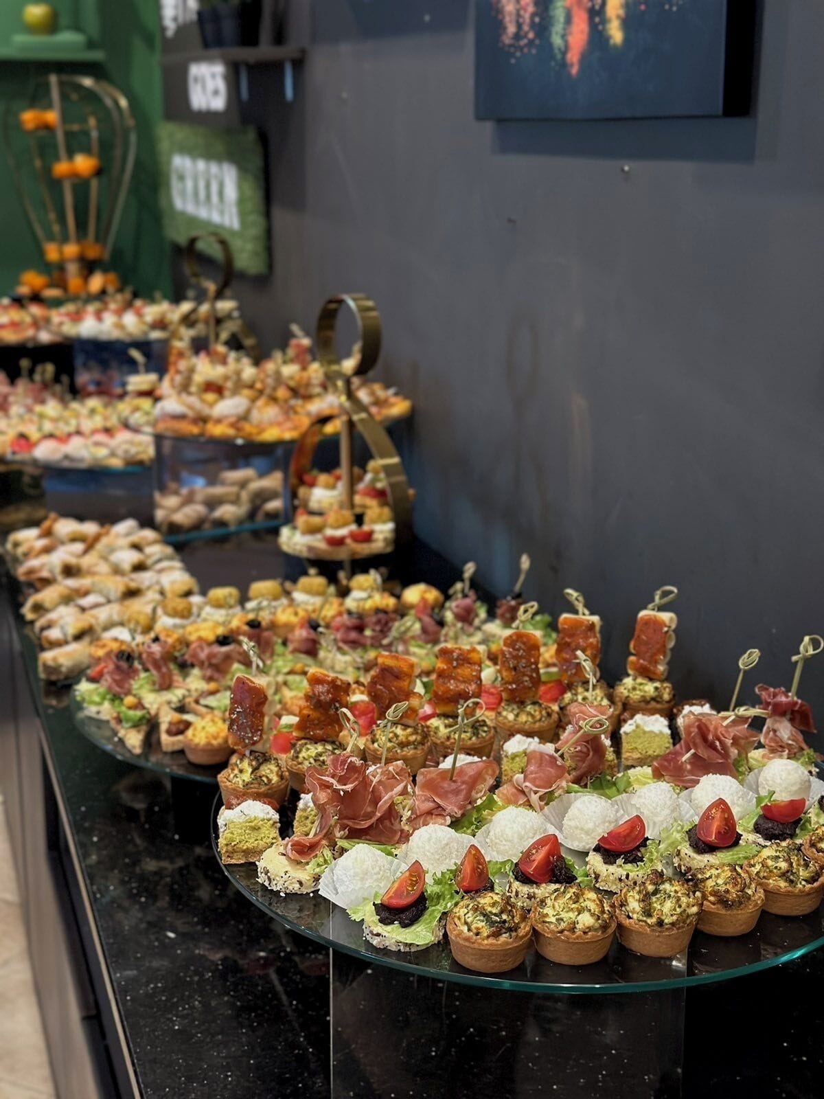 Ein Buffet mit verschiedenen Vorspeisen, darunter Mini-Quiches und Spieße, präsentiert auf einer Glasplatte.