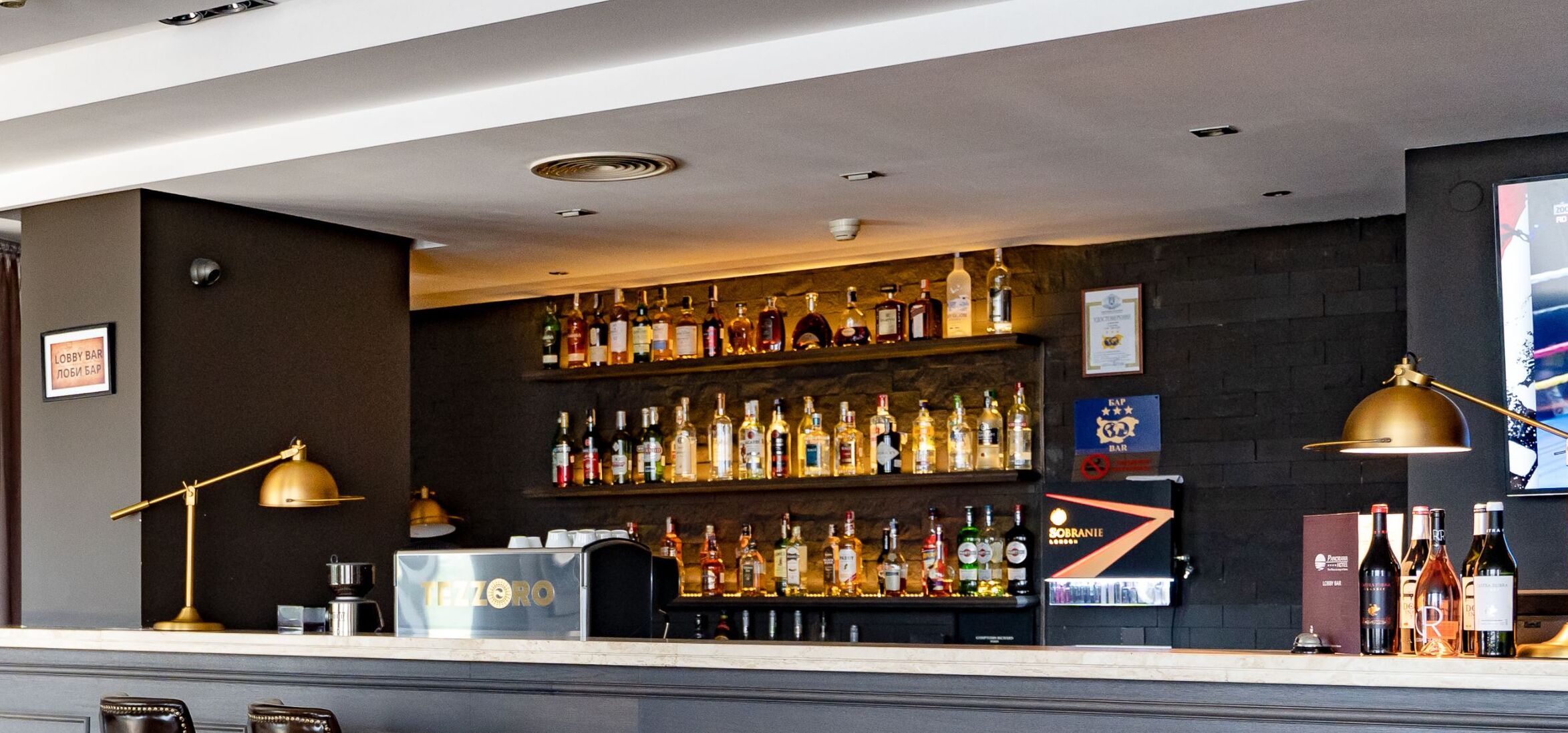 Een bar met flessen drank, een koffieapparaat en een bord met de tekst 'LOBBY BAR'.