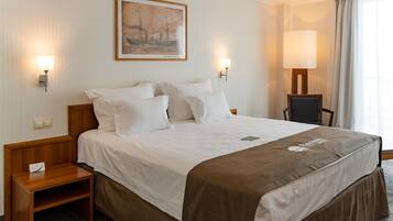 Habitación de hotel con una cama grande, dos mesitas de noche, una silla, un cuadro en la pared y dos lámparas de pared.