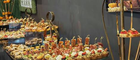 Un bufé con diversos alimentos expuestos en bandejas de vidrio y un atril de varios niveles.