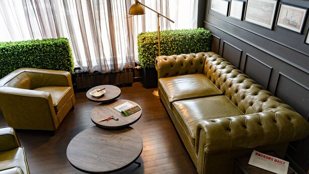 A modern lounge area with leather sofas, round tables, and a green hedge. - Hotel Panorama (Varna)
