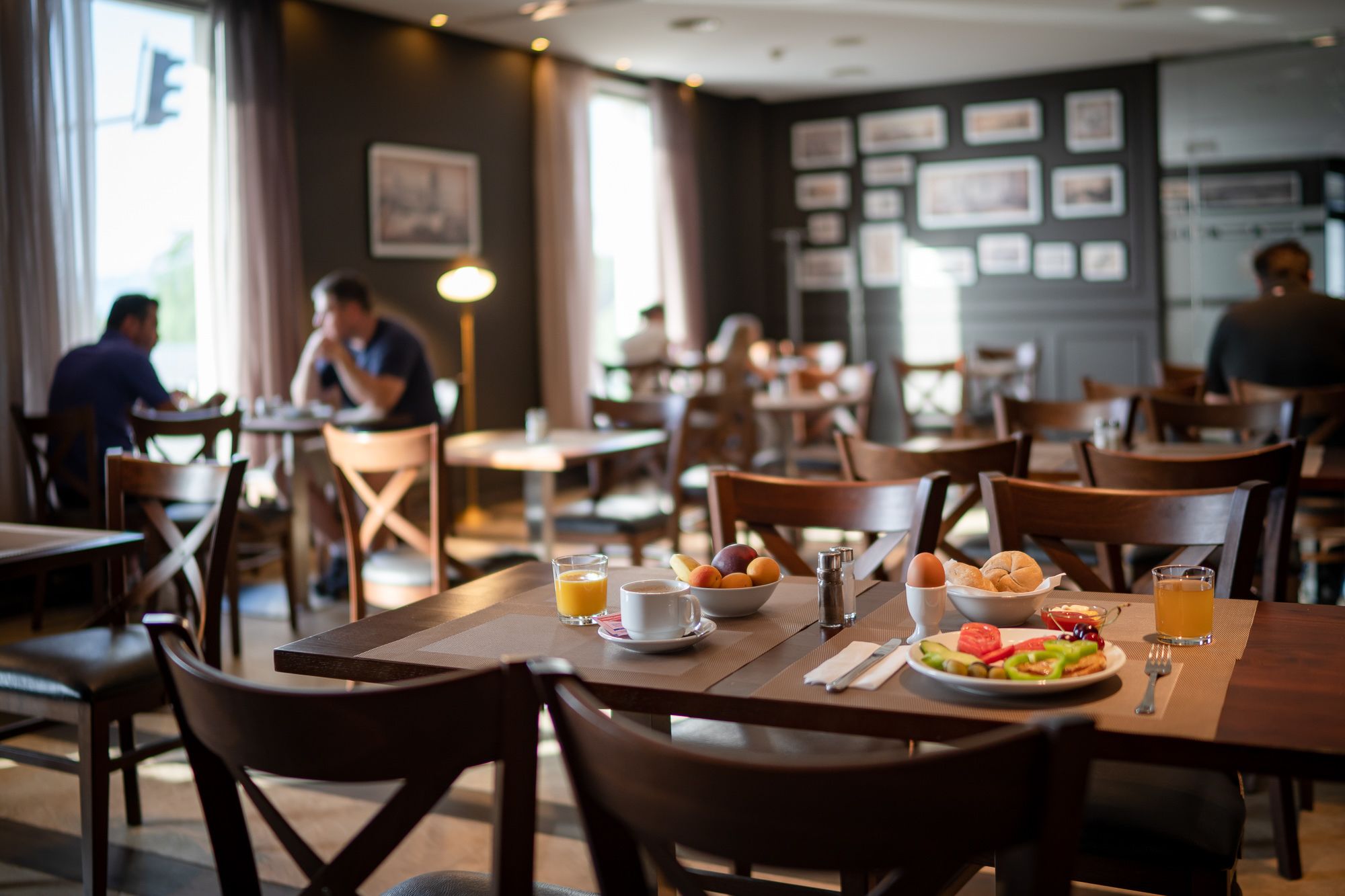 A restaurant with wooden tables and chairs, a breakfast spread including eggs, toast, and fruit, and framed pictures on the wall.