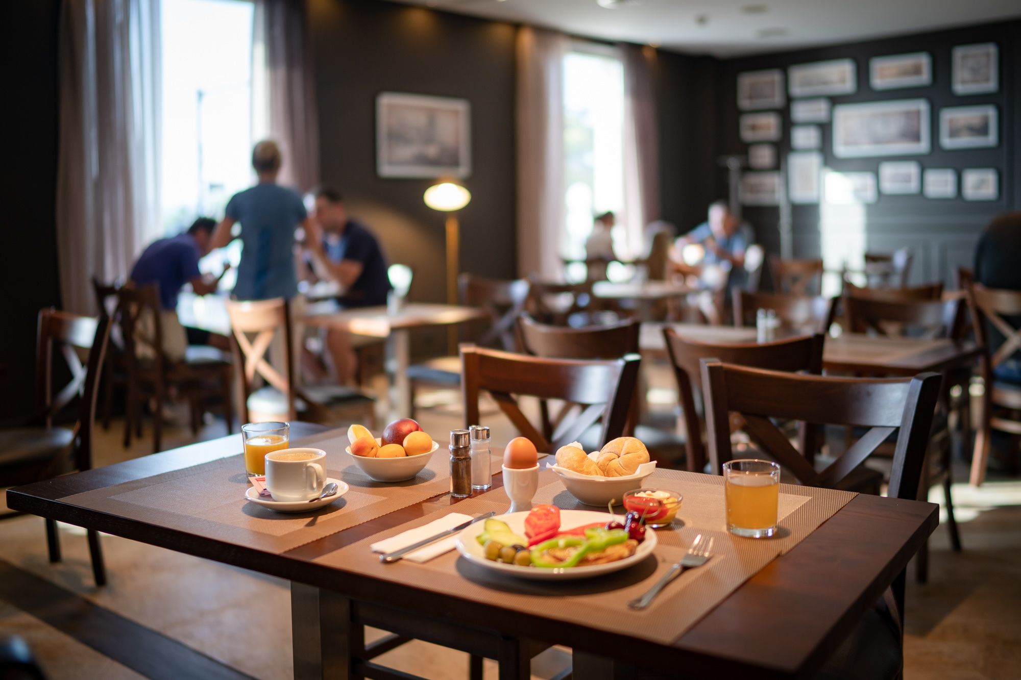 A restaurant with wooden tables and chairs, a variety of food and drinks on the tables, and framed pictures on the walls.