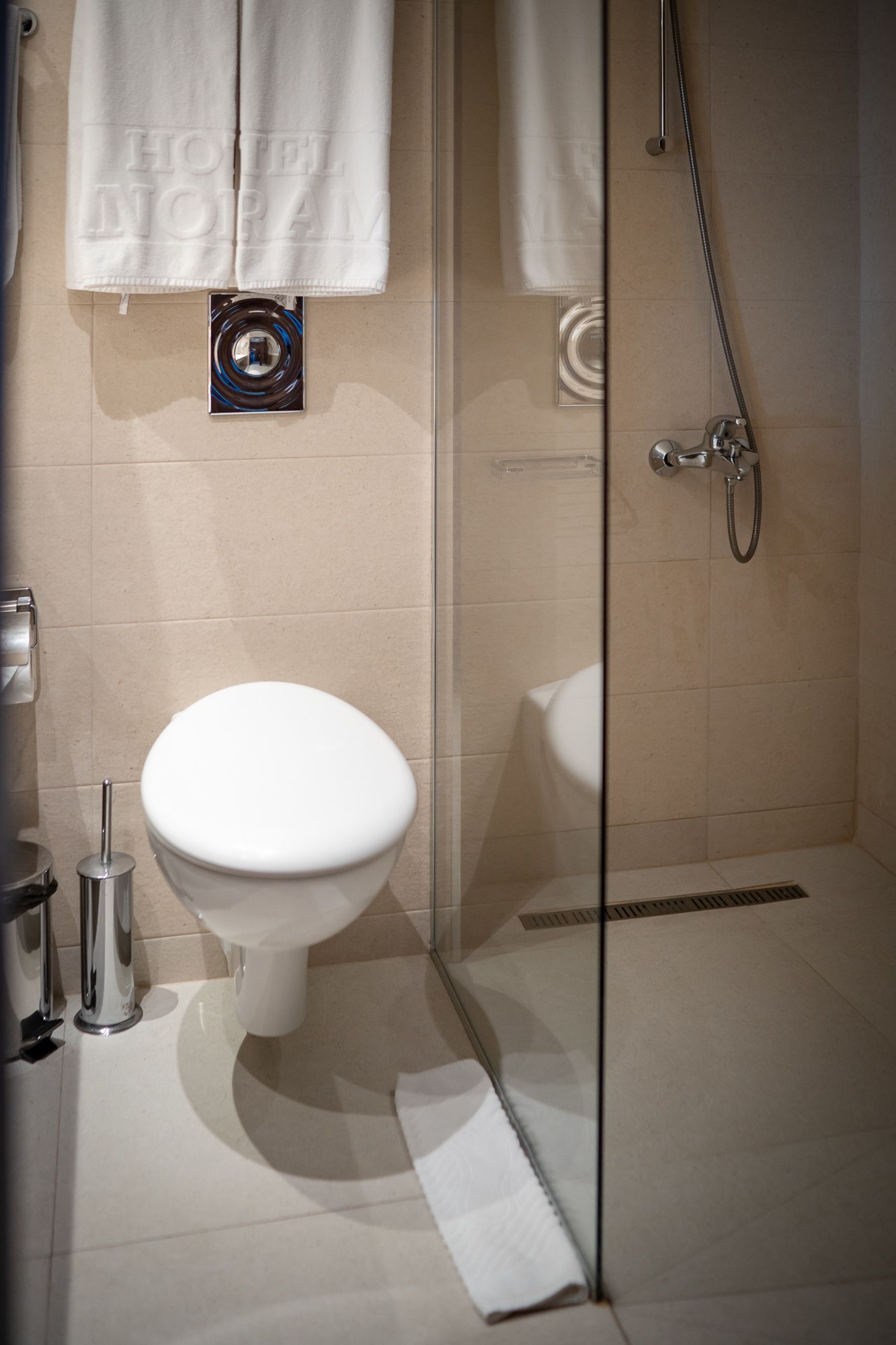 Un baño moderno con inodoro, cabina de ducha de vidrio y un perchero con toalla.