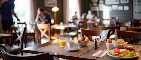 A dining area with tables set for breakfast, including plates of food, a bowl of fruit, and a cup of coffee.