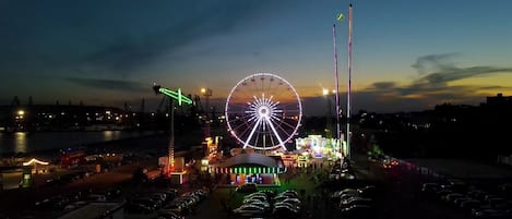 A Ferris wheel at dusk with a parking lot in the foreground.