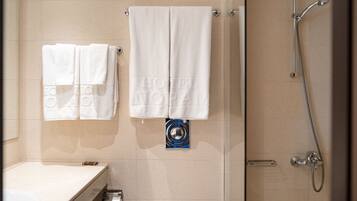 A bathroom with two white towels hanging on hooks, a toilet paper holder, and a shower with a handheld showerhead.