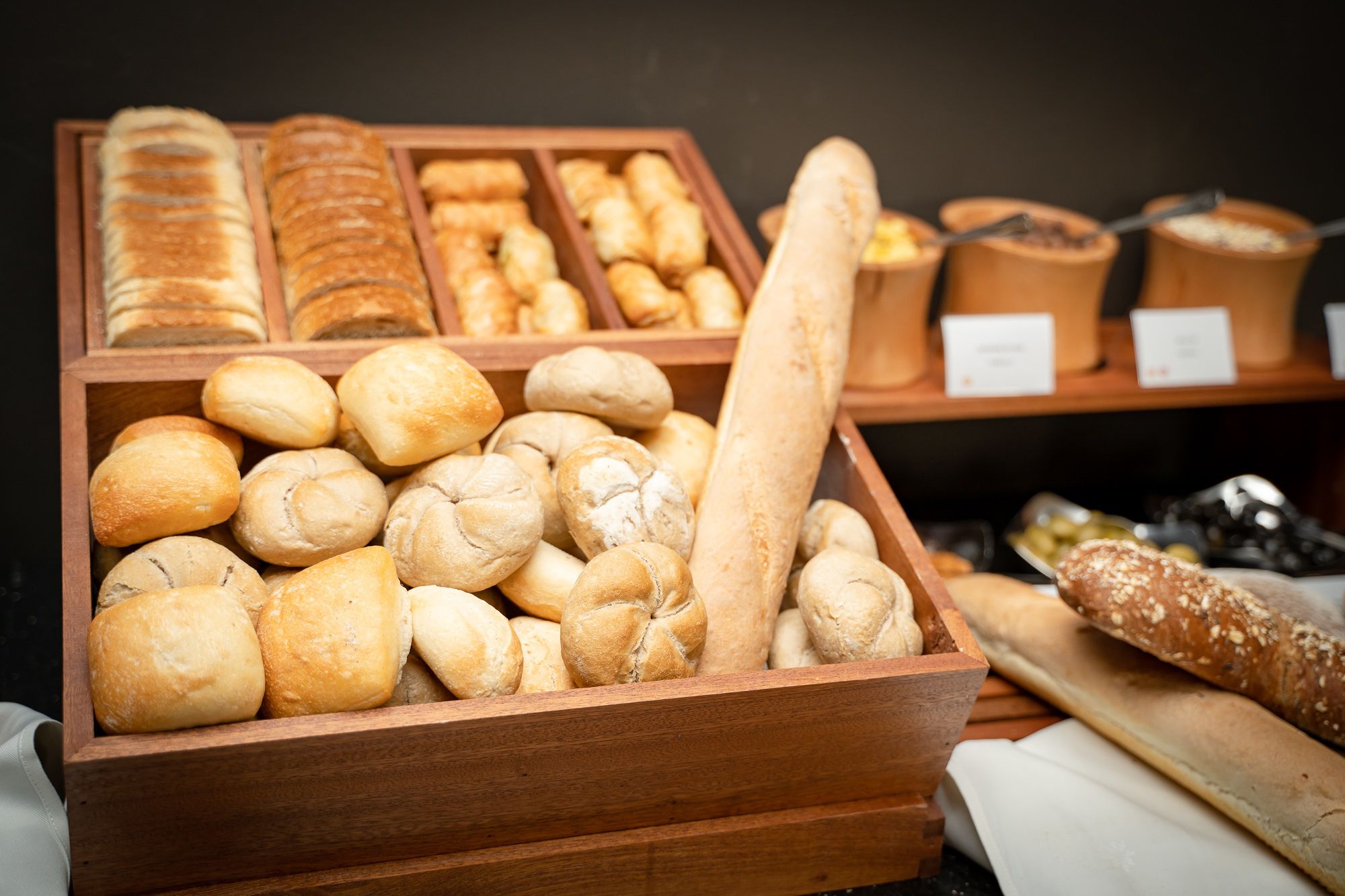 A wooden display case filled with various types of bread, including rolls, baguettes, and loaves.