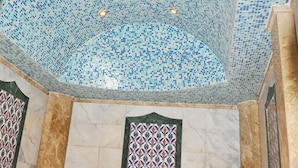 A bathroom with a mosaic-tiled ceiling, marble walls, and a red and white patterned towel.