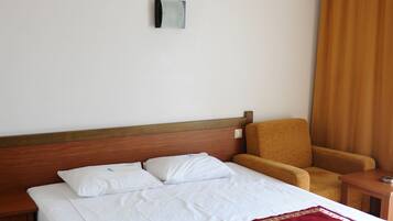 A hotel room with a large bed, a wooden headboard, a red throw blanket, a wooden nightstand, and a chair.