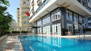 A swimming pool with lounge chairs and a building with balconies in the background.