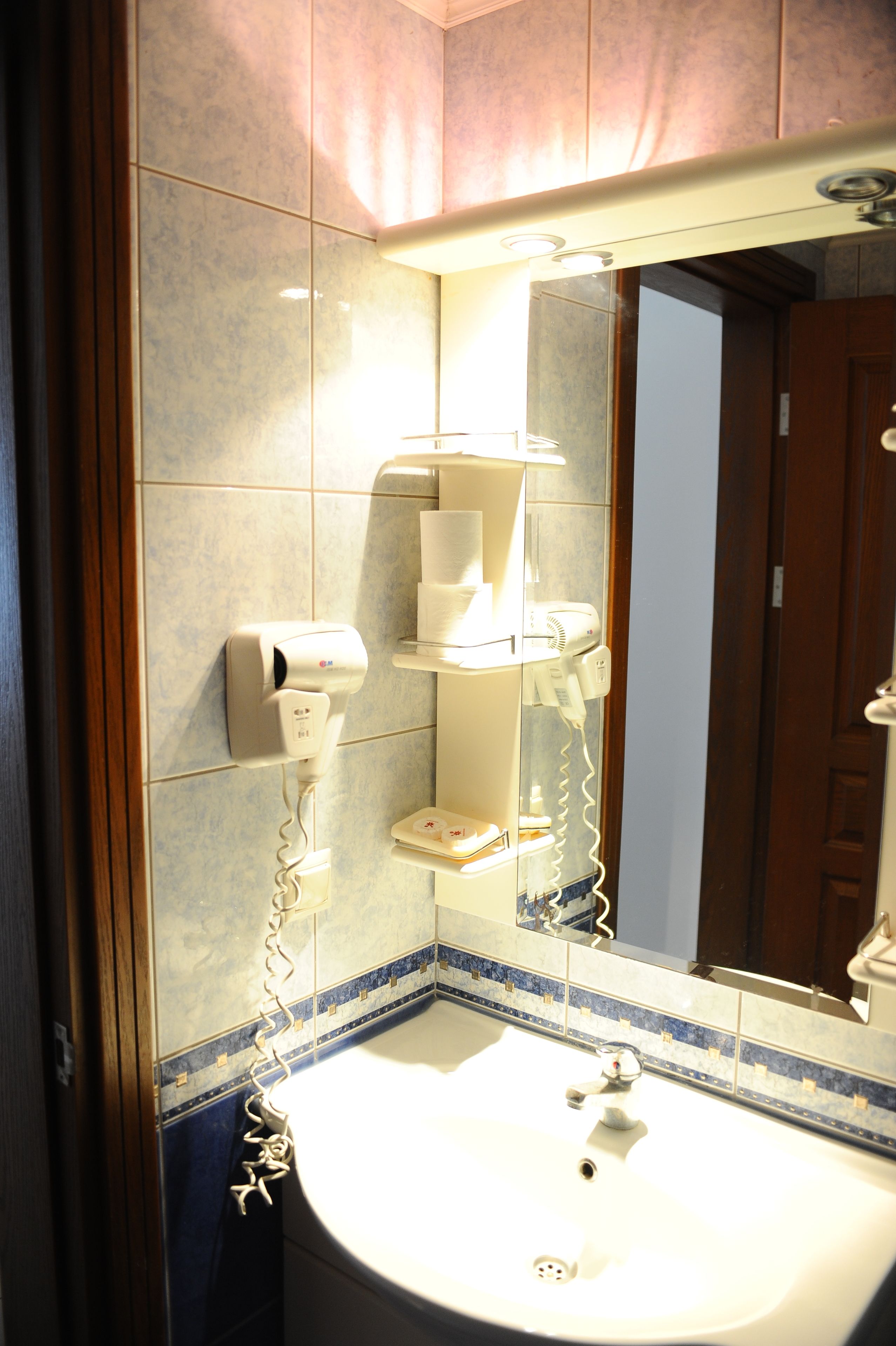 Un baño con lavamanos, espejo y secador de pelo fijado en la pared.