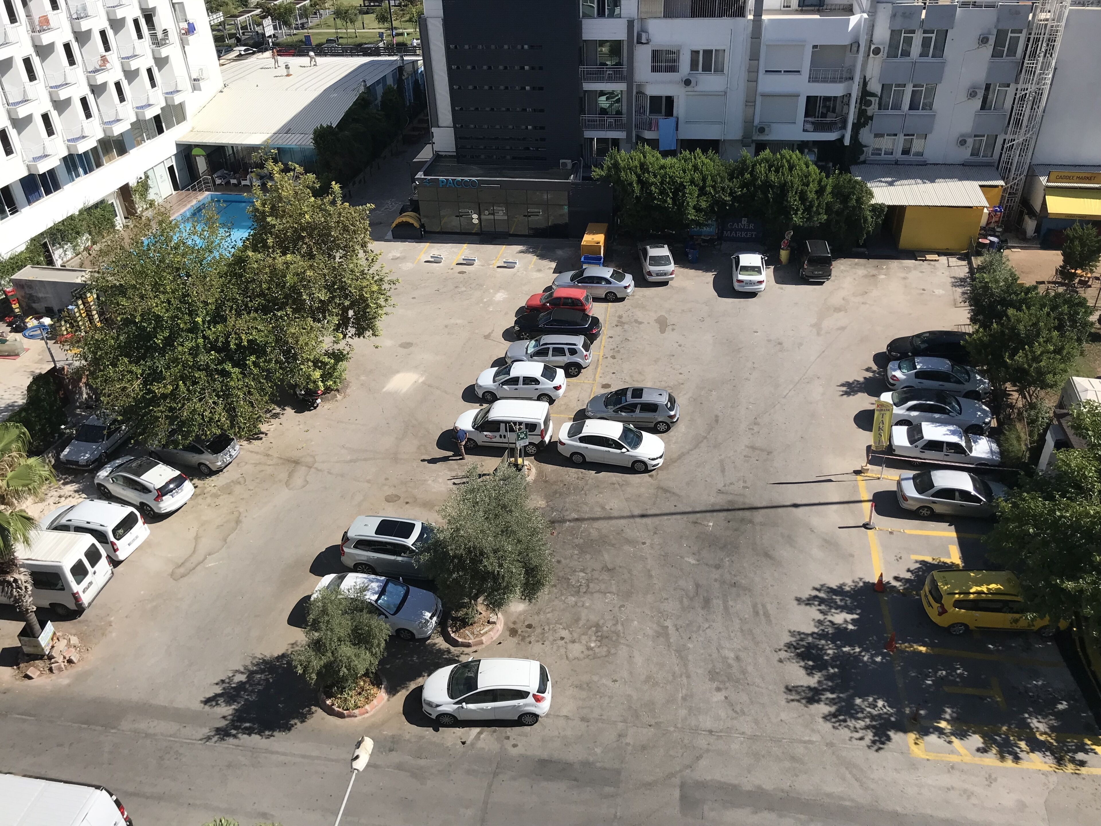 An aerial view of a parking lot with multiple cars and a few buildings in the background.