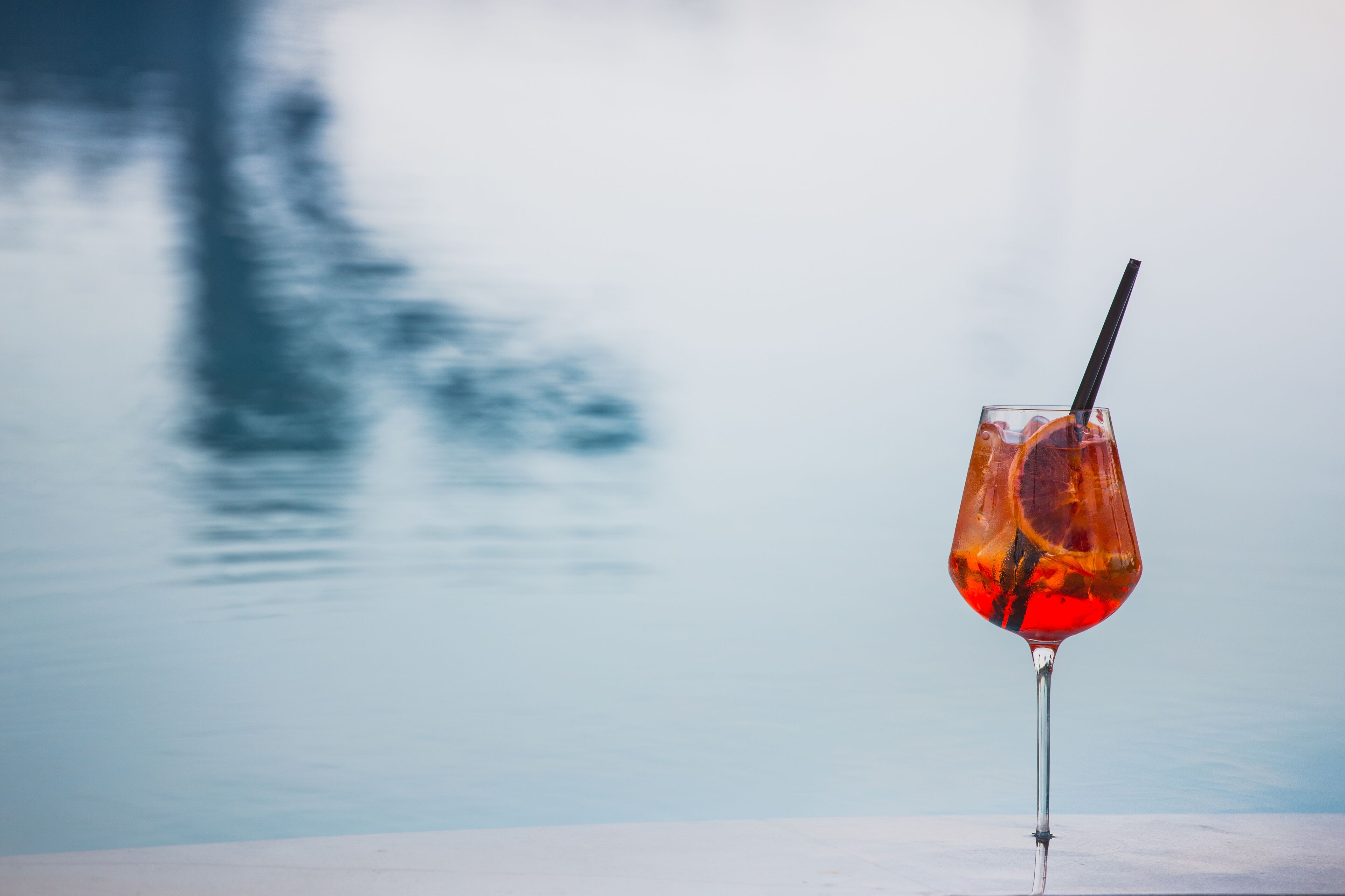 A glass with a straw and a slice of orange in it, placed on a table with a blurred background.