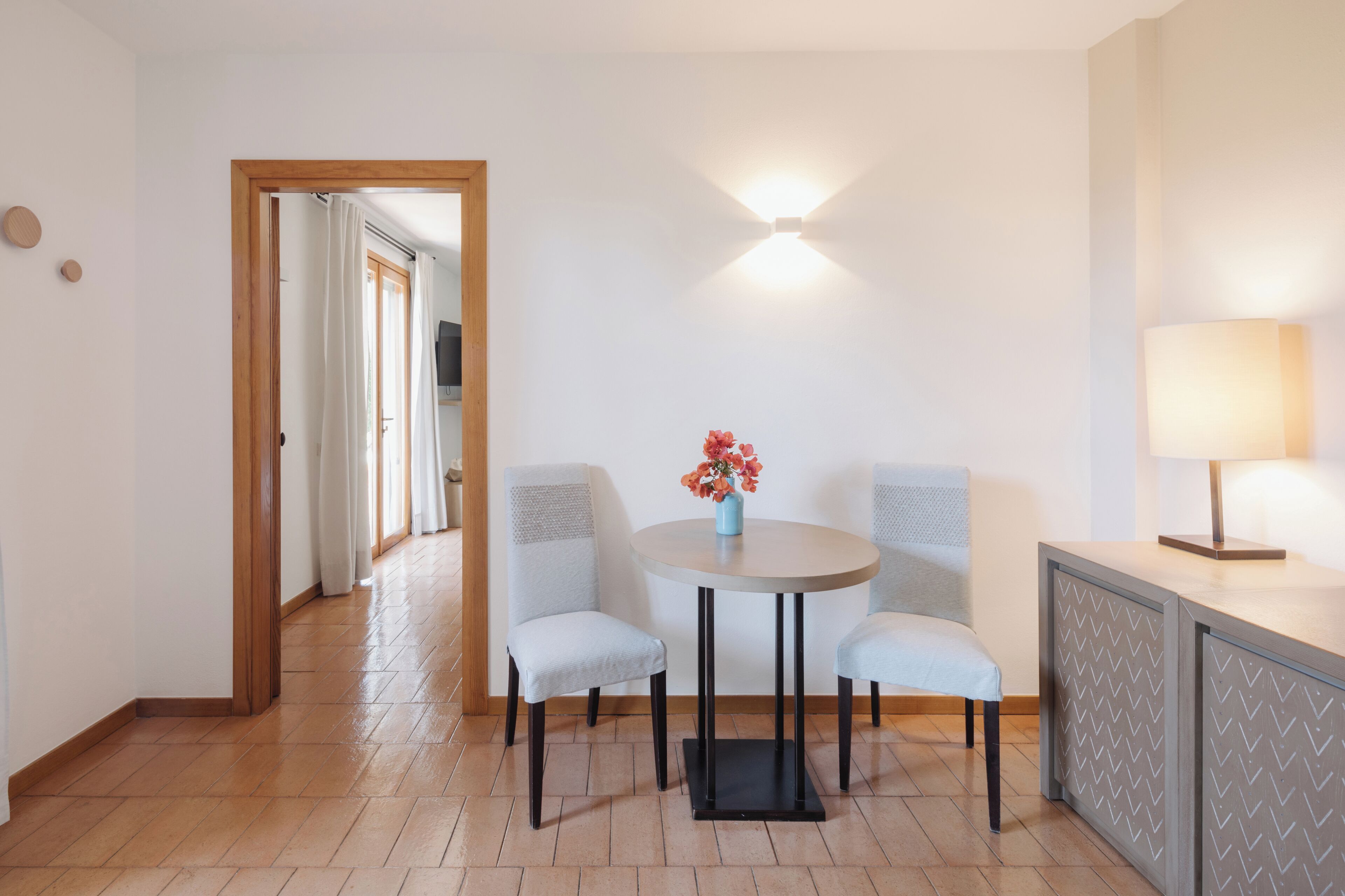 Ein Zimmer mit einem runden Tisch, zwei Stühlen, einer Blumenvase, einer Lampe und einer Wandleuchte.