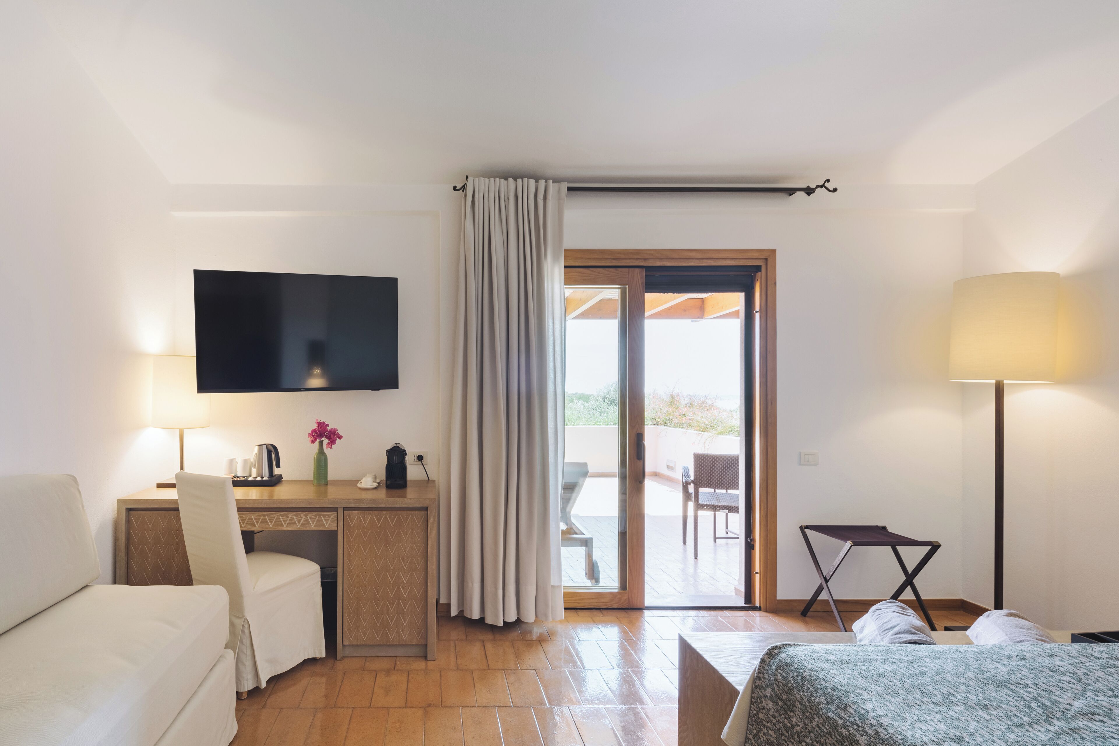 Hotelkamer met een bed, een bureau met stoel, een televisie, een lamp en een schuifdeur naar buiten.