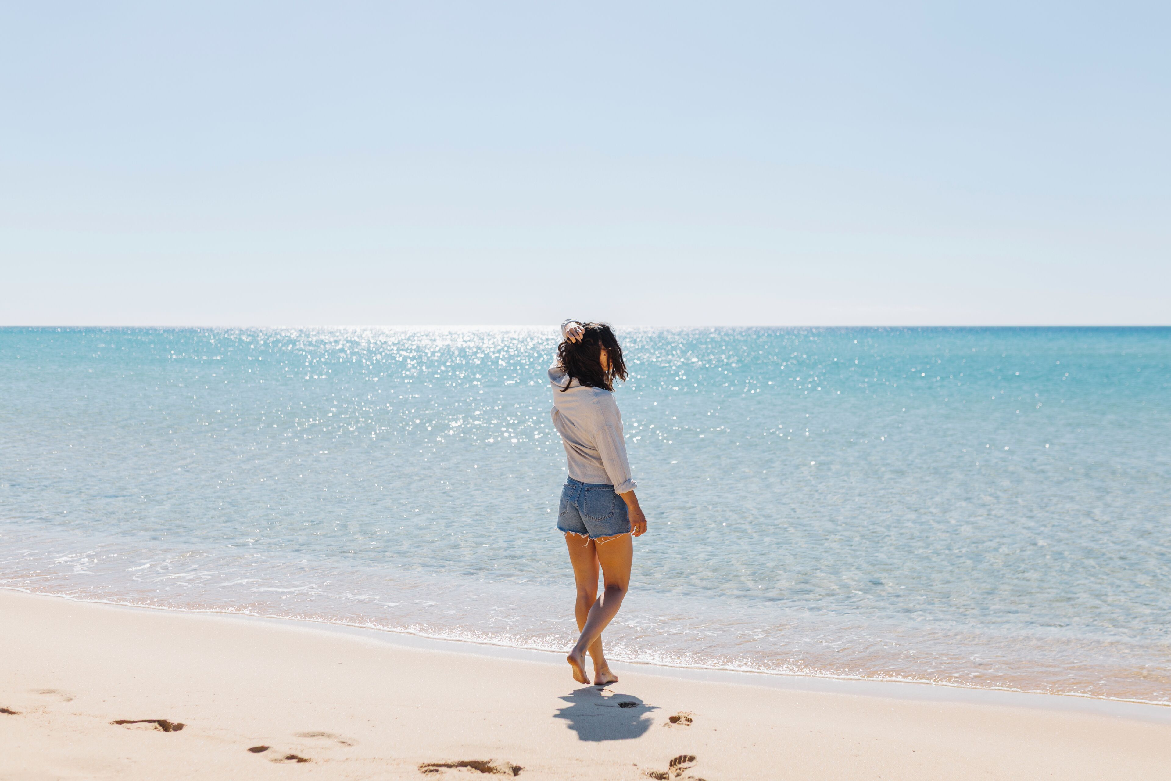 A person walking on a beach with a clear sky and calm sea.