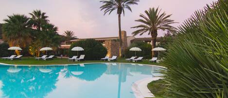 A pool with lounge chairs and palm trees.