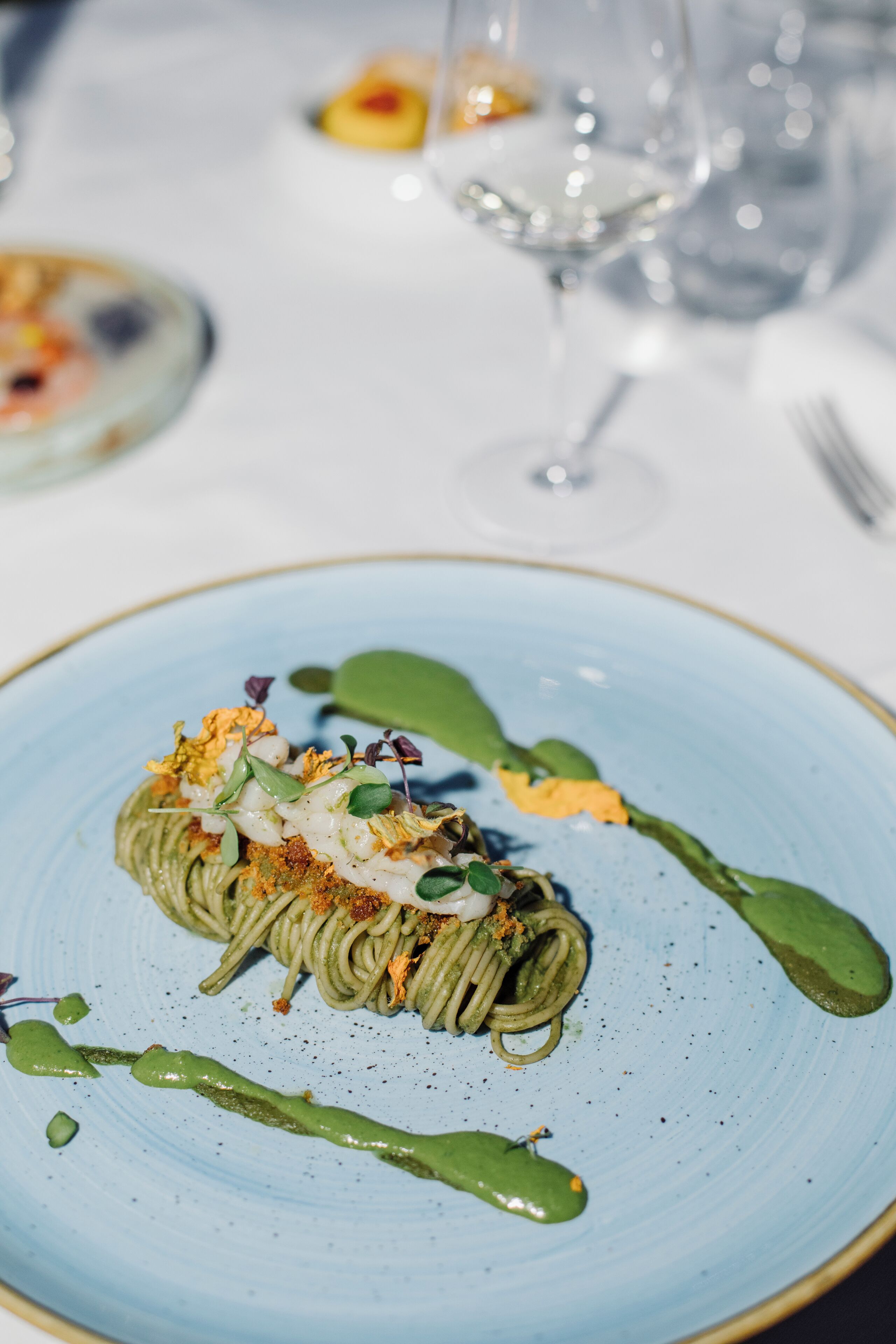 Un plato azul con un plato de pasta verde, adornado con hierbas y un chorrito de salsa verde.