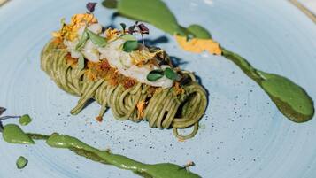 Un plato azul con un plato de pasta verde, adornado con hierbas y un chorrito de salsa verde.