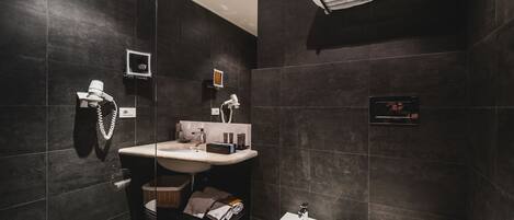 A modern bathroom with dark tiles, a white sink, a bidet, and a towel rack.
