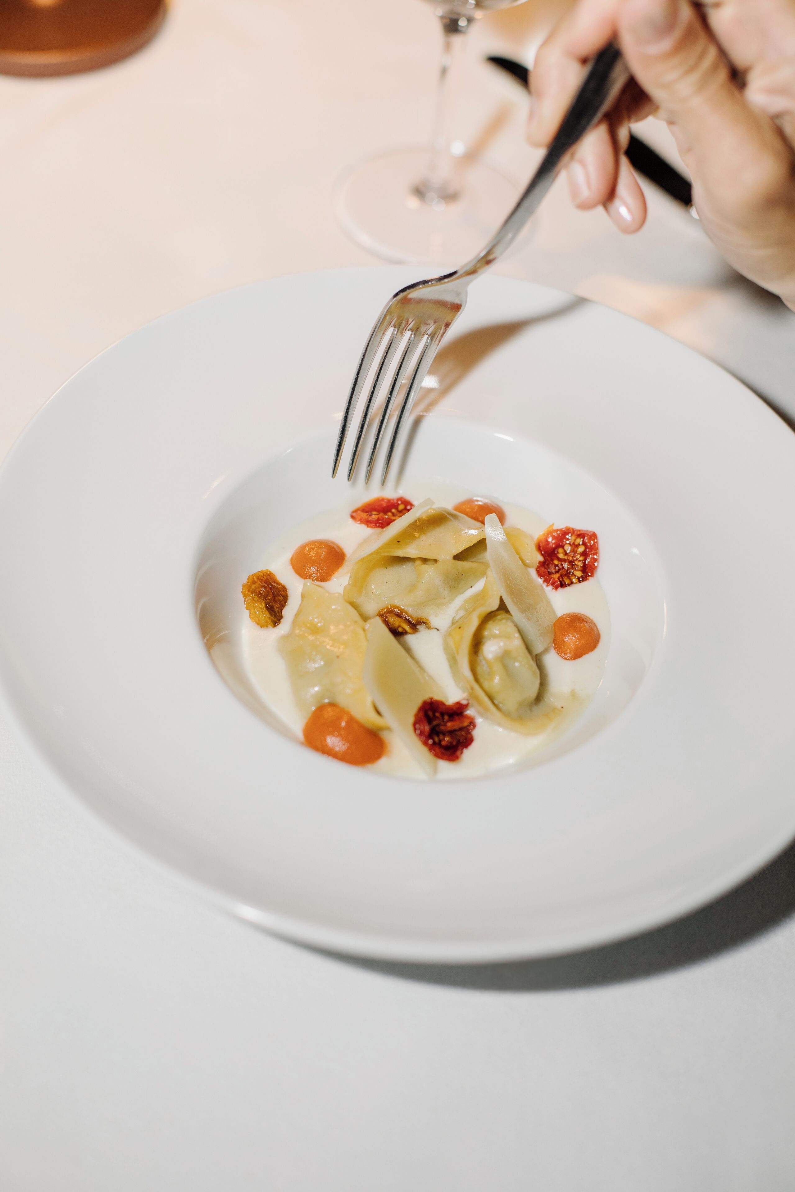Un plato blanco con ravioles, tomates cherry y una cuchara.