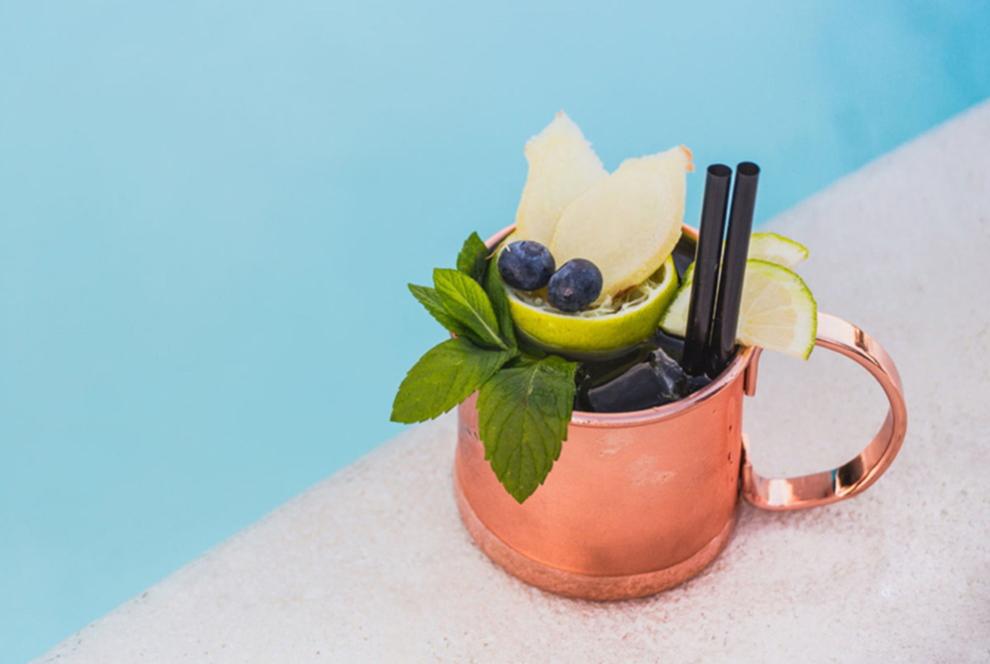 Ein Kupferbecher mit einem Getränk, Minzblättern, Blaubeeren und einer Limettenscheibe.