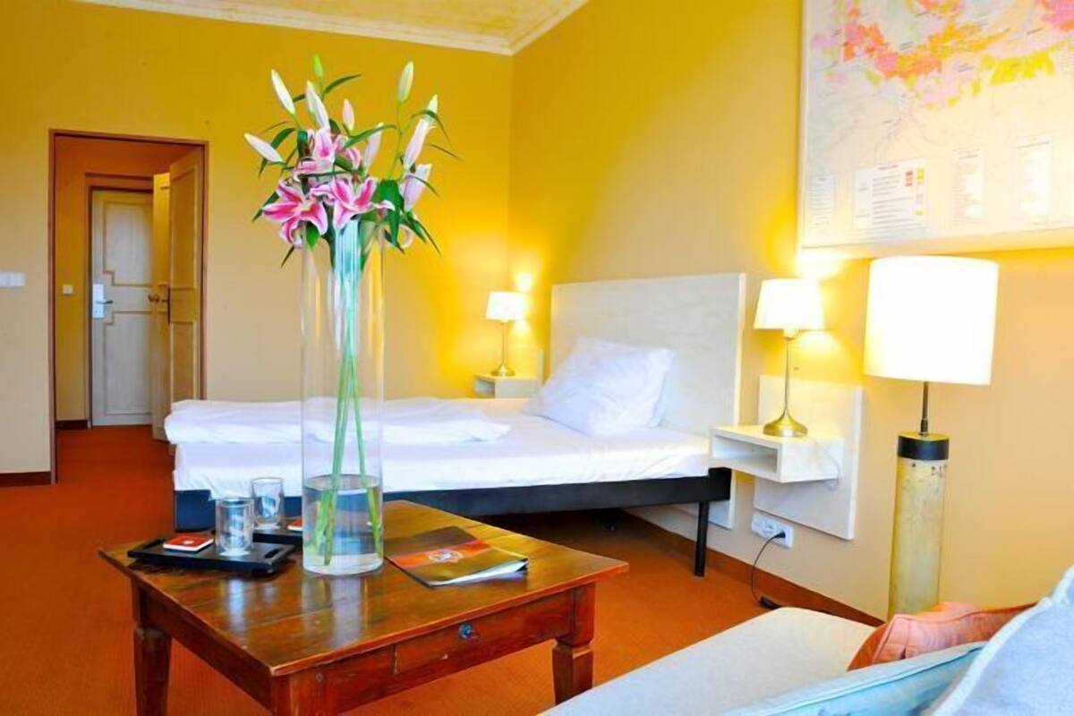 Habitación de hotel con cama, lámparas de mesita de noche, una mesita de madera, un florero con flores, una bandeja con vasos y un libro, y un mapa en la pared.