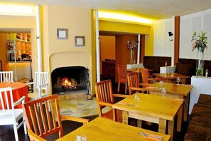 A cozy restaurant with wooden tables and chairs, a fireplace, and a bookshelf in the background. - Villa St. Tropez (Prague)
