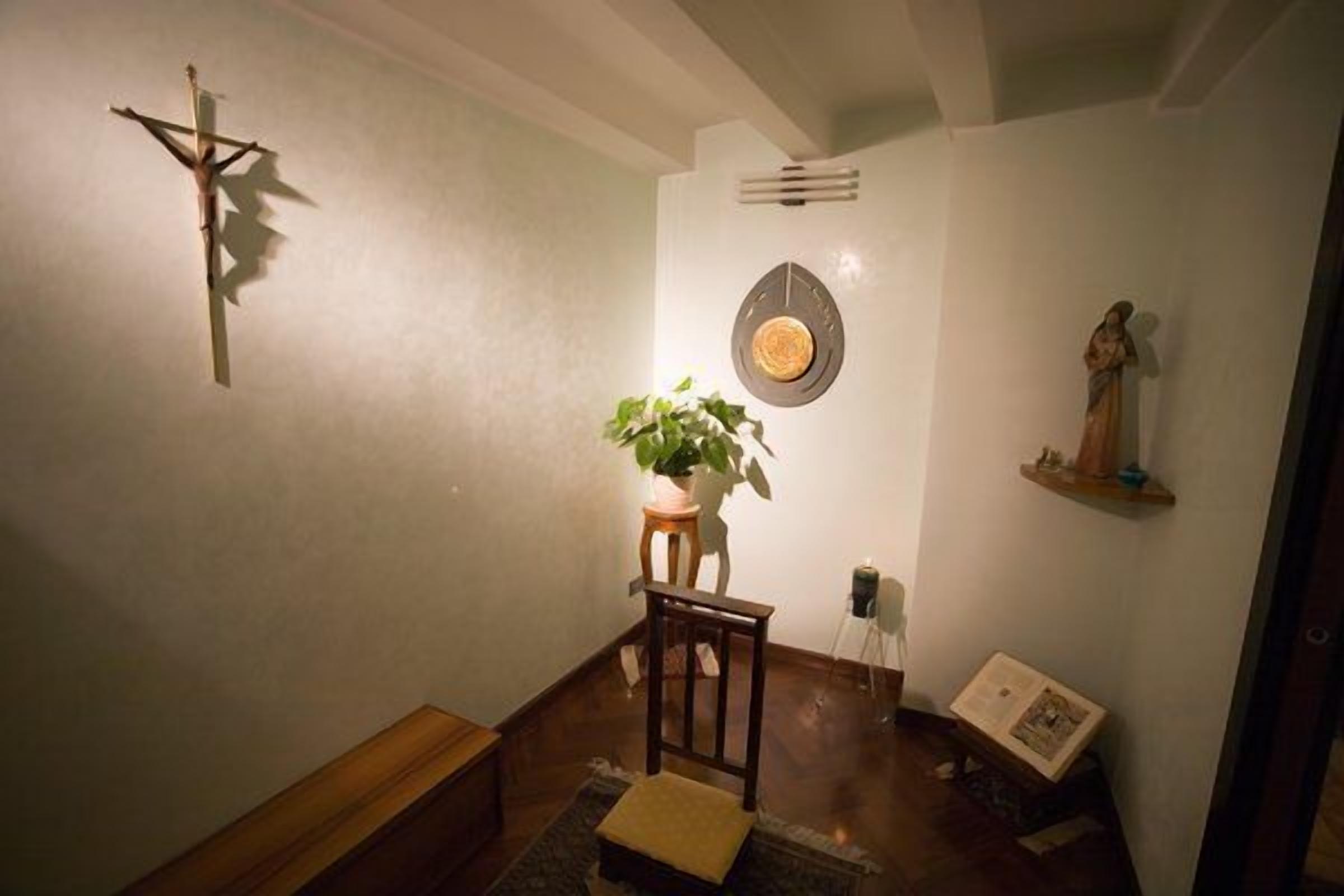 Une pièce comprenant un banc en bois, une petite table avec une plante, un élément de décoration fixé au mur et une statue posée sur une étagère.