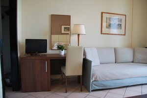 A hotel room with a wooden desk, a television, a lamp, a sofa, and a framed picture on the wall.