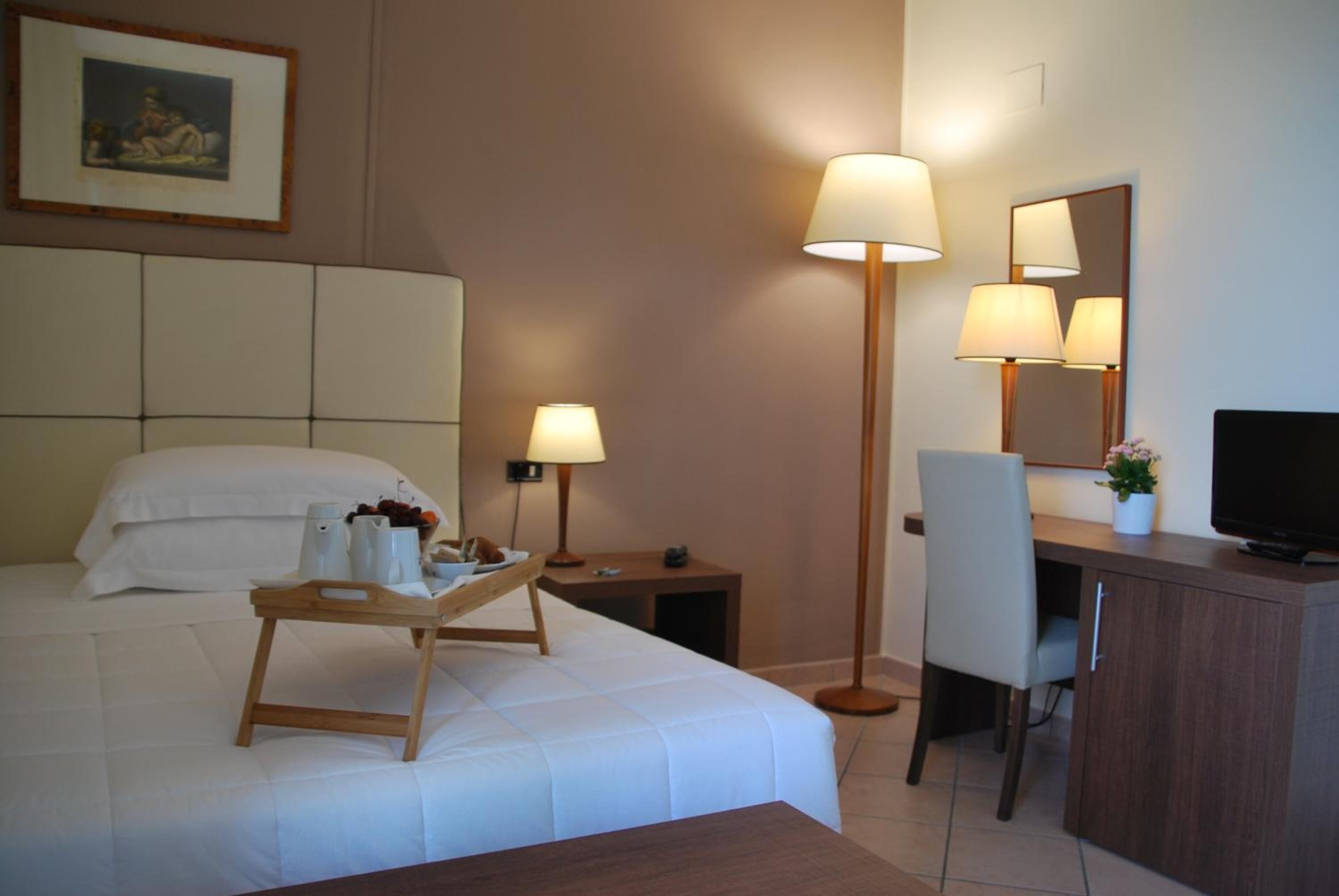 Una habitación de hotel con cama, mesitas de noche, un escritorio con silla, televisor y una lámpara de pie.