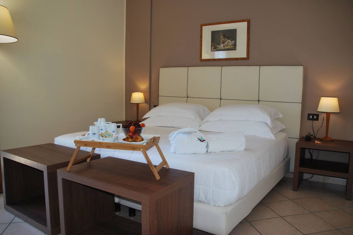 A hotel room with a bed, bedside tables, and a tray with breakfast items.