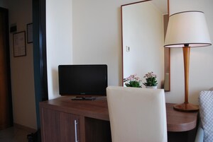 Hotellihuone, jossa on puinen työpöytä, litteänäyttöinen televisio, peili, lamppu ja pieni ruukkukasvi.