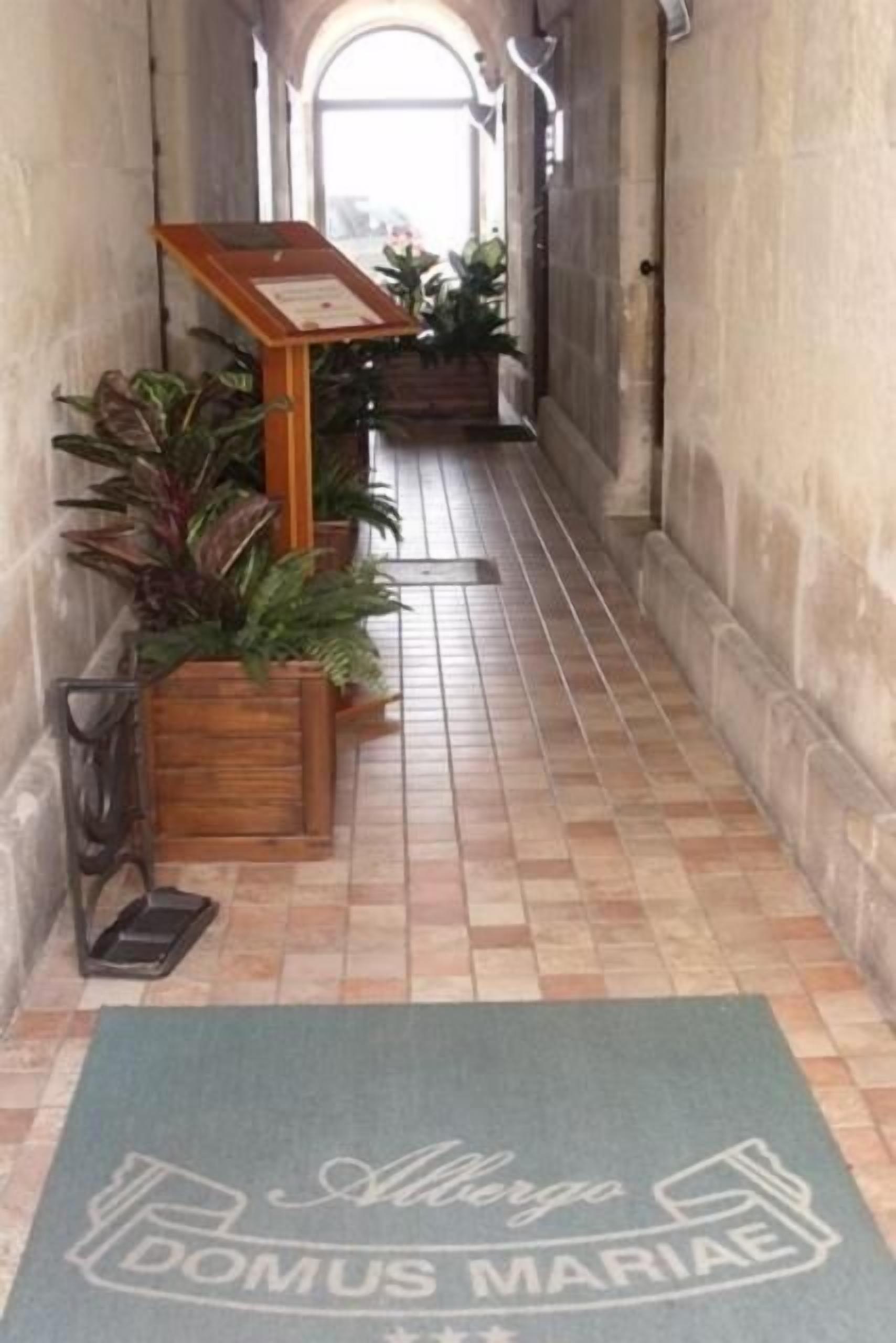 Un pasillo estrecho con suelo de baldosas, macetas de madera con plantas verdes y un cartel.