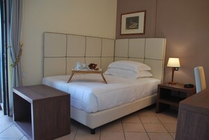 Habitación de hotel con cama, mesita de noche, lámpara y una pequeña mesita de madera con una bandeja de objetos.