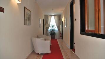 A hotel hallway with a red carpet, a white armchair, and framed pictures on the walls.