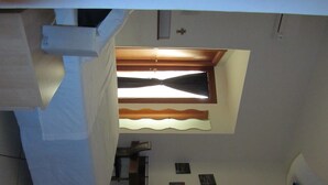 Una habitación con techo inclinado, una ventana con marco de madera y una pequeña mesa con una silla.