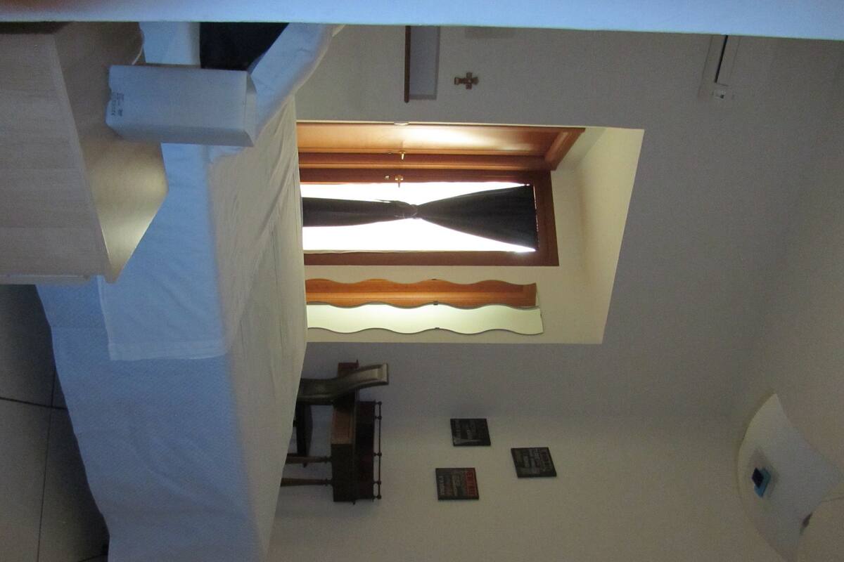 A room with a sloped ceiling, a window with a wooden frame, and a small table with a chair.