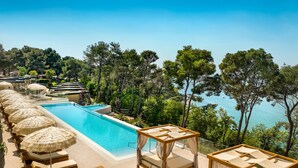 Zona junto a la piscina con sillones de descanso y sombrillas, con vista a una masa de agua rodeada de árboles.