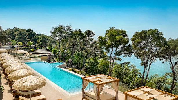 A poolside area with lounge chairs and umbrellas, overlooking a body of water and surrounded by trees. - Valamar Camping Lanterna (Tar-Vabriga)