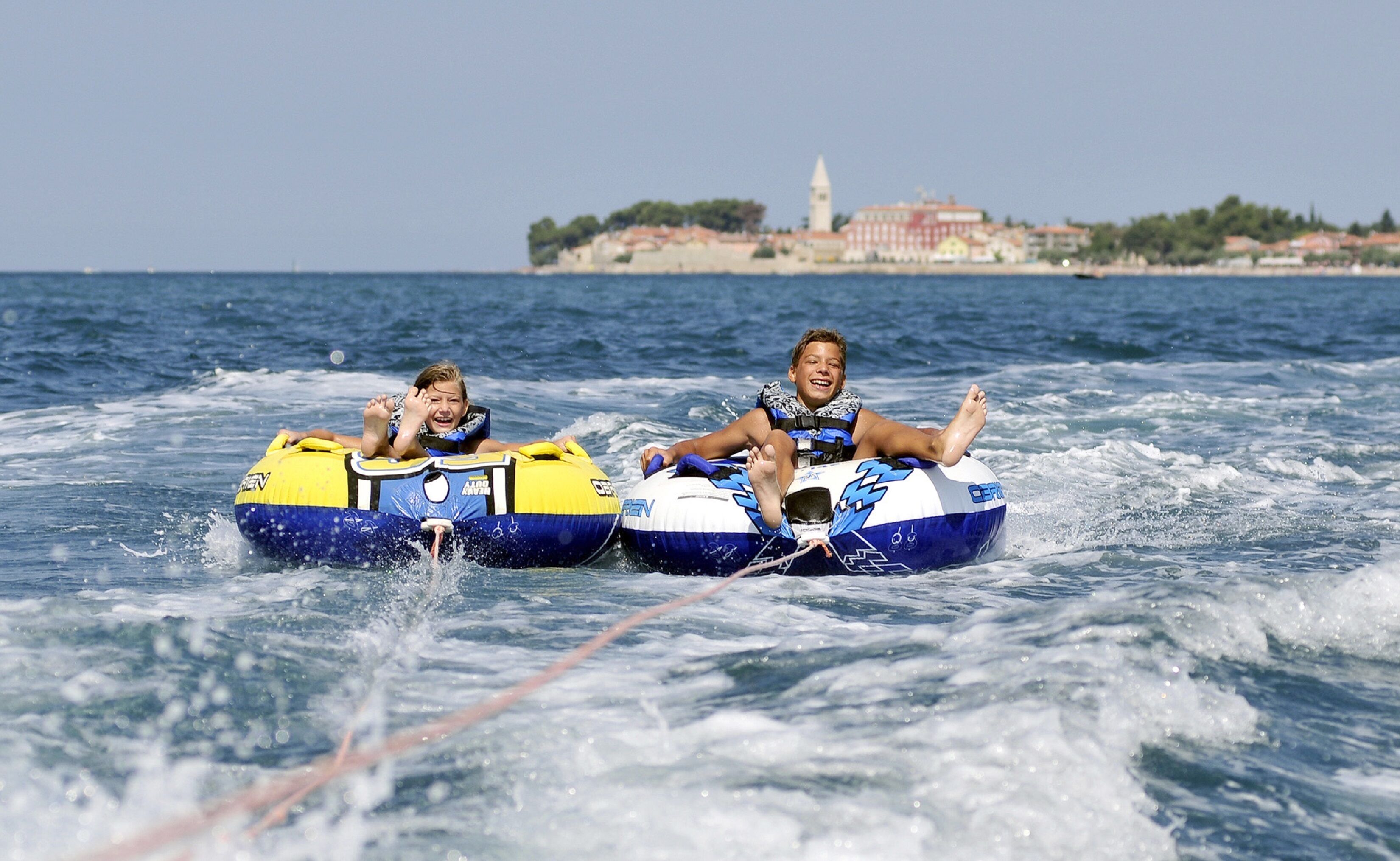 Two people on watercrafts with a coastal town in the background.