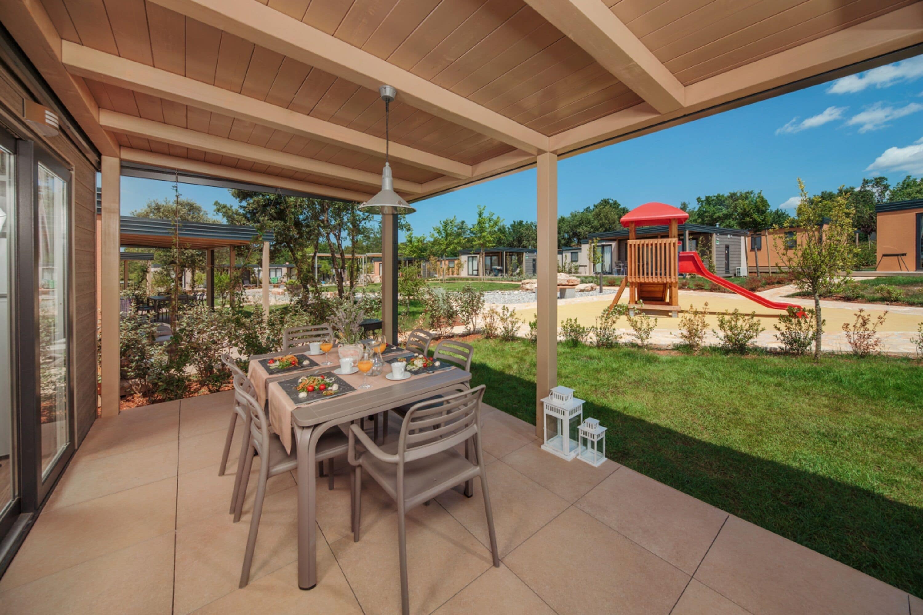 A covered patio with a dining table and chairs, a hanging light fixture, and a view of a playground with a slide and play structures.
