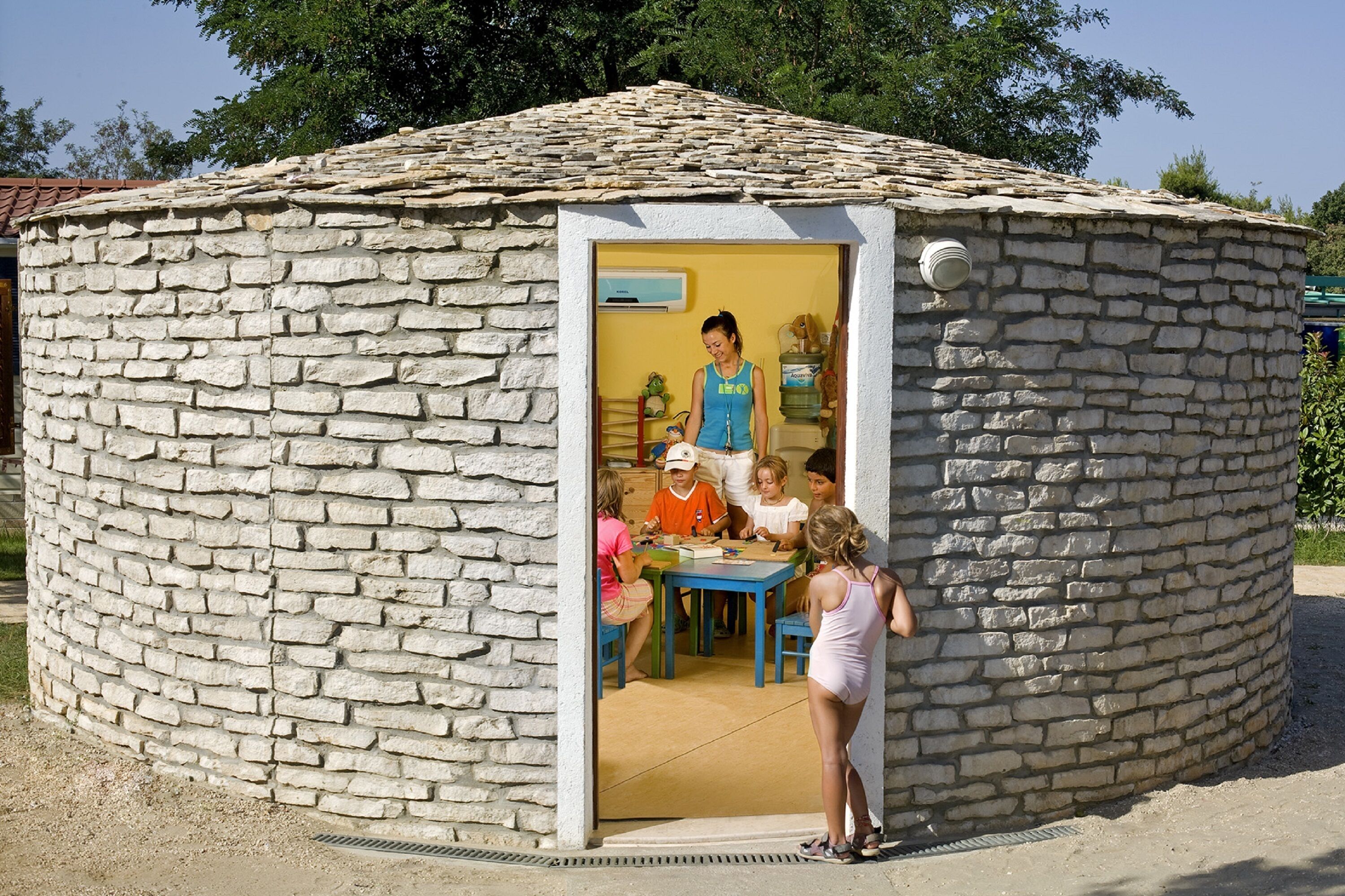 A stone-built structure with a circular shape and a tiled roof. Inside, there is a table with chairs and a person standing.
