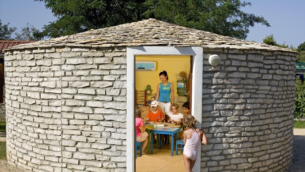 Una estructura de piedra con forma circular y techo de tejas. En el interior, hay una mesa con sillas y una persona de pie.