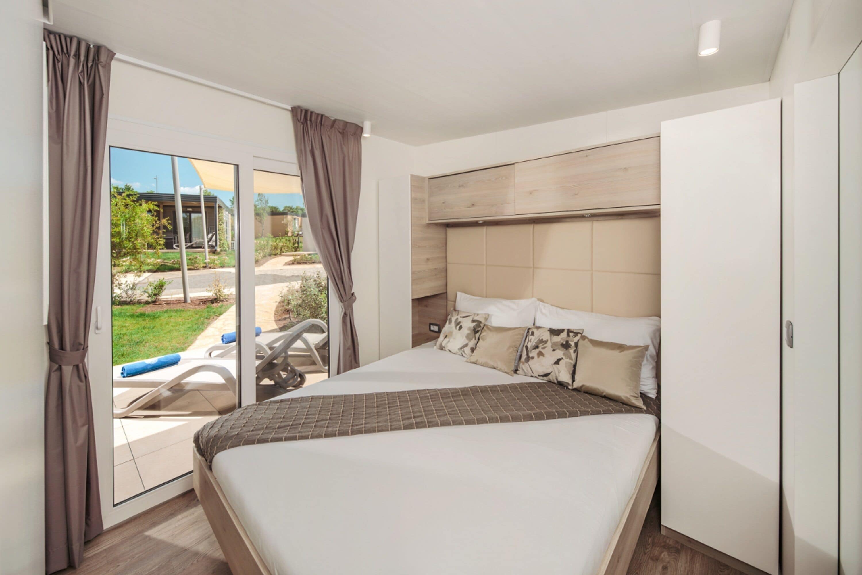 A modern bedroom with a large bed, a sliding glass door to a balcony, and a wooden headboard.
