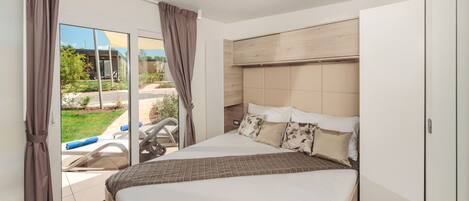 A modern bedroom with a large bed, a sliding glass door to a balcony, and a wooden headboard.