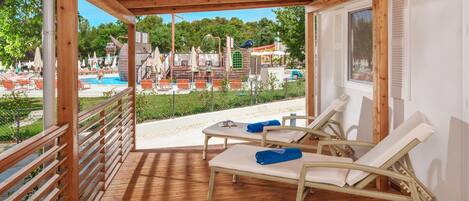Una terraza de madera con dos sillones de descanso y una piscina al fondo.